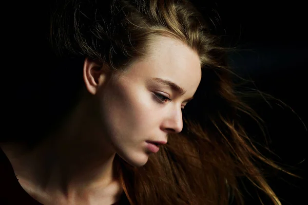 Hermosa chica mirando a un lado, de perfil, pelo volando. Drama. Fotografía de estudio en bajo perfil sobre un fondo oscuro —  Fotos de Stock