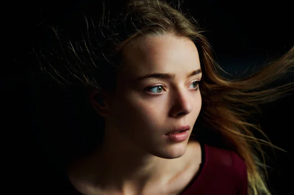 Mooi meisje op zoek naar de kant, in profiel, haar vliegen. Drama. Studiofotografie in lage sleutel op een donkere achtergrond — Stockfoto