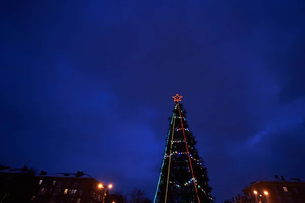 Decorated Christmas tree with a red star  the glowing lights against the dark blue sky — Stock Photo, Image