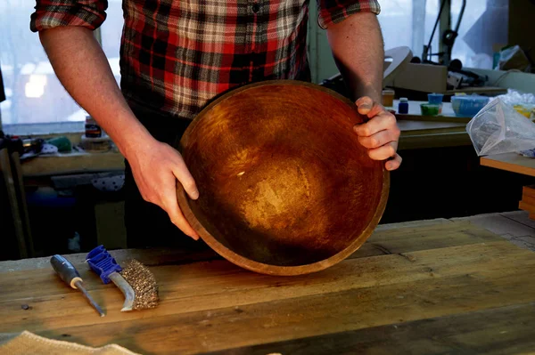 Чоловічі руки тримають дерев'яну велику миску. Обробка поверхні в майстерні . — стокове фото