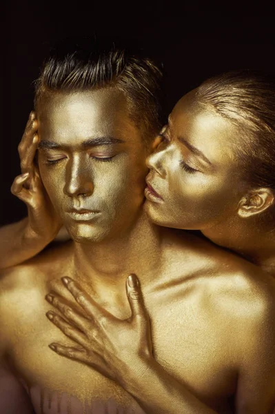 A girl and a guy covered in gold paint. With my eyes closed. The girl leaned in and kisses his ear — Stock Photo, Image