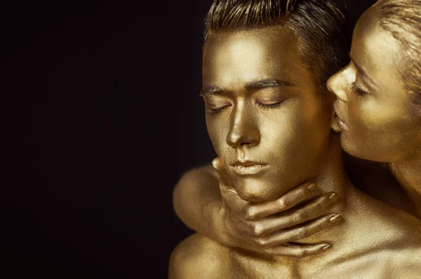 A girl and a guy covered in gold paint. With my eyes closed. The girl leaned in and kisses his ear — Stock Photo, Image