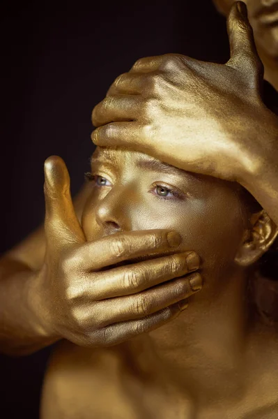 Een meisje en een jongen, bedekt met gouden verf. Het gezicht van de grote meid. De jonge man die handen op gezicht: lippen en voorhoofd. De spanning, de beperking van de persoonlijke vrijheid — Stockfoto