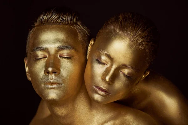 Male and female face around. The womans head lies on the shoulder of a man.All painted in gold paint, the feeling of a single whole organism. — Stock Photo, Image