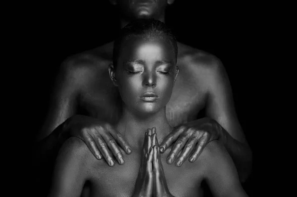 A young girl, covered in gold paint. Hands are clasped in Buddhist prayer. Supplication, request. On the shoulders of mens hands, Black and white — Stock Photo, Image