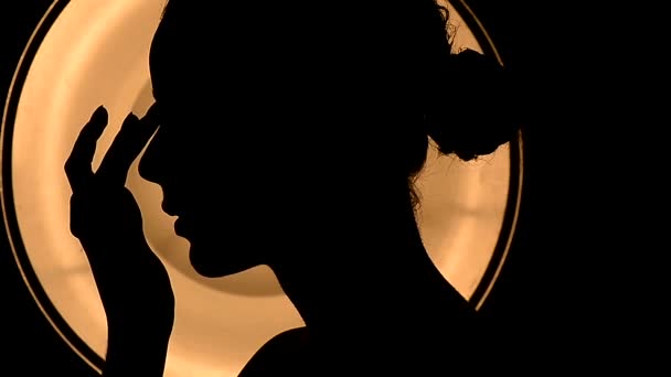 Das schlanke Mädchen berührte ihr Gesicht. Dutt-Frisur. Aufnahme einer Silhouette gegen das warme Licht. schließen — Stockvideo
