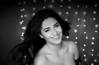 Uzun saçlı esmer gülümseyen güzel bir portresi. Stüdyo fotoğrafçılığı, bokeh ampulleri. Siyah ve beyaz