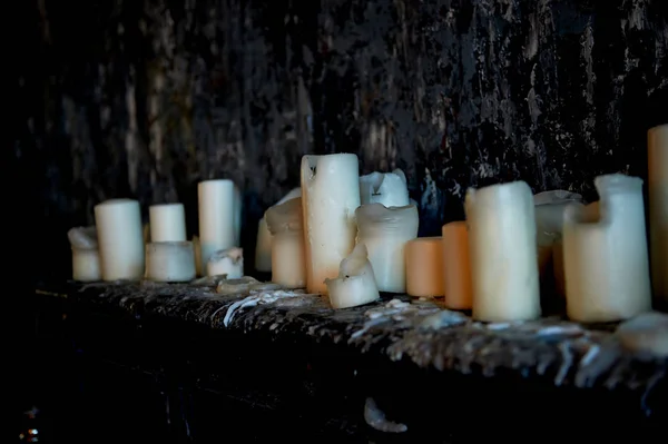 Lilin berdiri di permukaan gelap terhadap dinding gelap, semua di lilin basah. Banyak lilin, api menyala. Lilin yang padam — Stok Foto