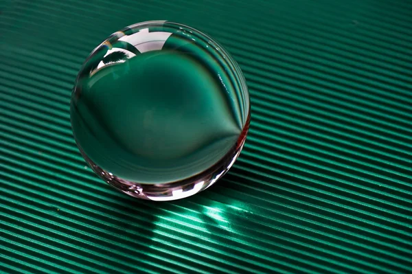 Glaskugel oder Wassertropfen auf einem Hintergrund aus grünem Wellpapier. — Stockfoto