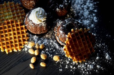 Taze çikolatalı kek ile pudra şekeri serpilir gür, koyu renk ahşap karşı koymak. Yuvarlak Belçika waffle. Ayrıca fındık fıstık var. Stüdyo