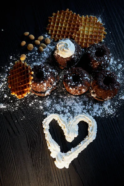 Exuberantes magdalenas de chocolate fresco espolvoreado con azúcar en polvo, poner contra la madera oscura. Gofres belgas redondos. También tienen cacahuetes de nueces. crema de corazón pintado. — Foto de Stock