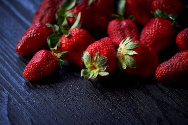 Koyu siyah ahşap arka plan üzerinde kırmızı sulu çilek. Su damlacıkları. Sululuk, vitaminler ve sağlıklı gıda