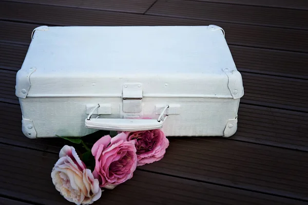 Valise blanche avec des fleurs roses contre un sol sombre . — Photo
