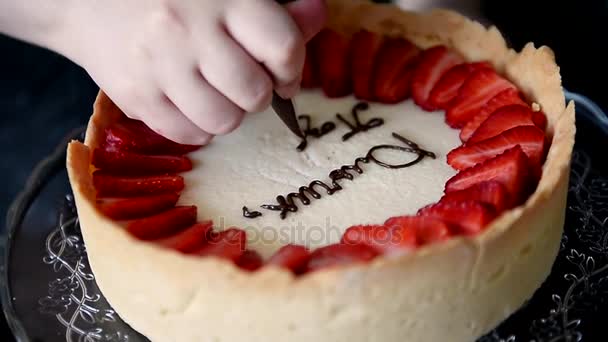Chef de pastelaria decora um cheesecake com inscrição de morangos com um saco de cozinha e creme marrom — Vídeo de Stock