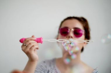 Yan görünümü atış sabun köpüğü beyaz arka plan üzerinde üfleme genç kadın modeli kapatın. Eller ve değnek odaklanmak.