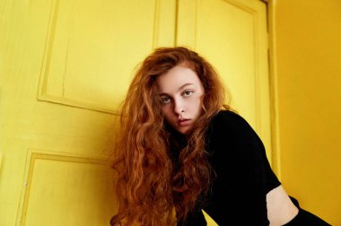 Model testleri. Kıvırcık saçlı güzel kızıl saçlı kız. Doğal renk. Sarı ahşap kapı ile harika kontrast