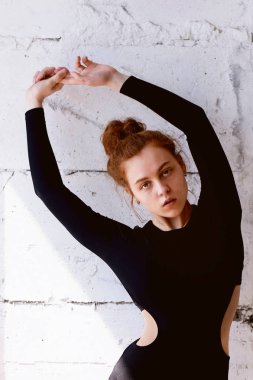 Model testleri. Kıvırcık saçlı güzel kızıl saçlı kız. Doğal renk. Yoga, aerobik ve tuğla duvar parlak arka plan üzerinde bale için esneklik gösterir. Studio-loft. Bir siyah giyimli