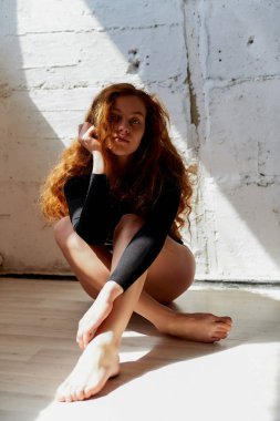 Model testleri. Kıvırcık saçlı güzel kızıl saçlı kız. Doğal renk. Yoga, aerobik ve tuğla duvar parlak arka plan üzerinde bale için esneklik gösterir. Studio-loft. Bir siyah giyimli