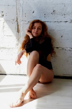 Model testleri. Kıvırcık saçlı güzel kızıl saçlı kız. Doğal renk. Yoga, aerobik ve tuğla duvar parlak arka plan üzerinde bale için esneklik gösterir. Studio-loft. Bir siyah giyimli