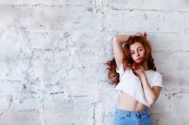 Model testleri. Kıvırcık saçlı güzel kızıl saçlı kız. Doğal renk. Standları hafif tuğla duvara üfleme uzun saçlı. Studio loft