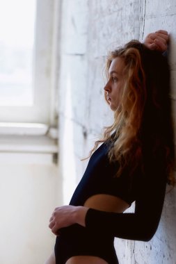 Model testleri. Kıvırcık saçlı güzel kızıl saçlı kız. Doğal renk. Yoga, aerobik ve tuğla duvar parlak arka plan üzerinde bale için esneklik gösterir. Studio-loft. Bir siyah giyimli