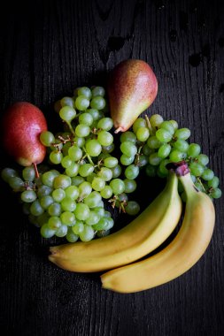 Karanlık bir arka plan üzerine taze meyve: üzüm, armut ve muz. Sağlıklı beslenme