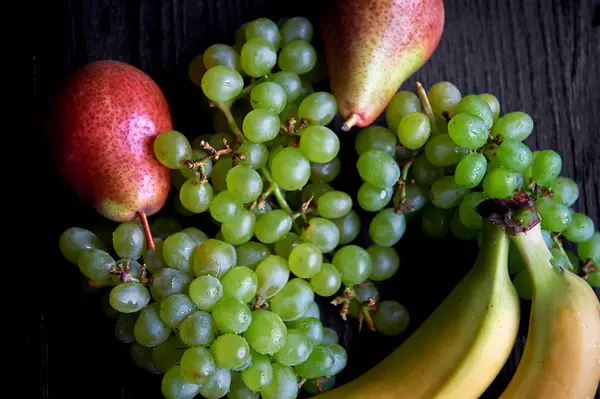 Fresh fruit on a dark background: grapes, pear and bananas.Healthy eating — Stock Photo, Image