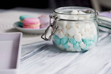 Marshmallow hafif ahşap yüzey üzerinde pastel renklerde beyaz ve mavi. Bir cam kavanozun içinde bir menteşeli kapak ile