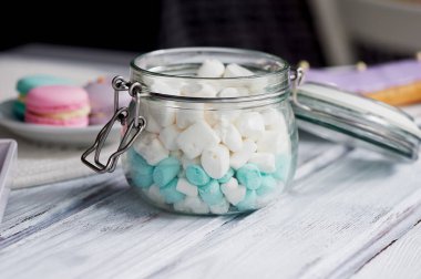 Marshmallow hafif ahşap yüzey üzerinde pastel renklerde beyaz ve mavi. Bir cam kavanozun içinde bir menteşeli kapak ile