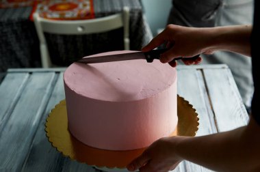 Pasta şefi pasta uzun bir bıçak ile kesmek. El bakımı. Süsler olmadan minimalist tarzda bir pembe pasta kesme.