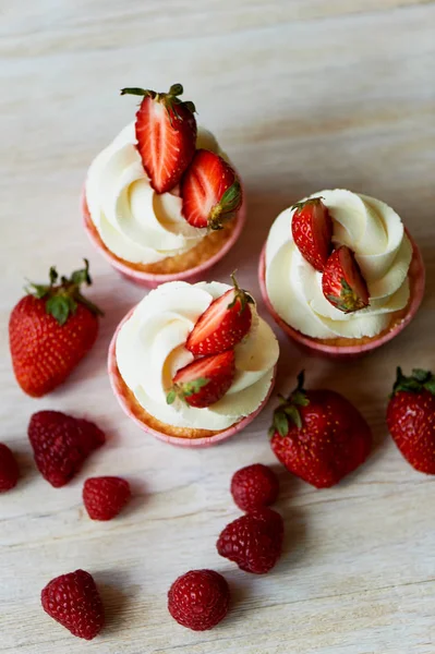 Cupcakes con crema batida y crema dulce, decorados con fresas. Sobre un fondo de madera claro . — Foto de Stock