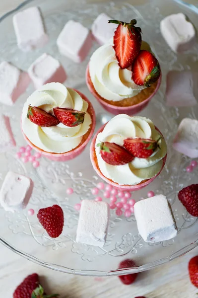 Cupcakes con crema batida y crema dulce, decorados con fresas. En un soporte de vidrio, con malvaviscos — Foto de Stock