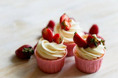 Krem şanti ve tatlı ile cupcakes krem, çilek ile dekore edilmiştir. Bir ışık ahşap arka plan üzerinde.