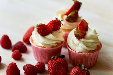 Krem şanti ve tatlı ile cupcakes krem, çilek ile dekore edilmiştir. Bir ışık ahşap arka plan üzerinde.