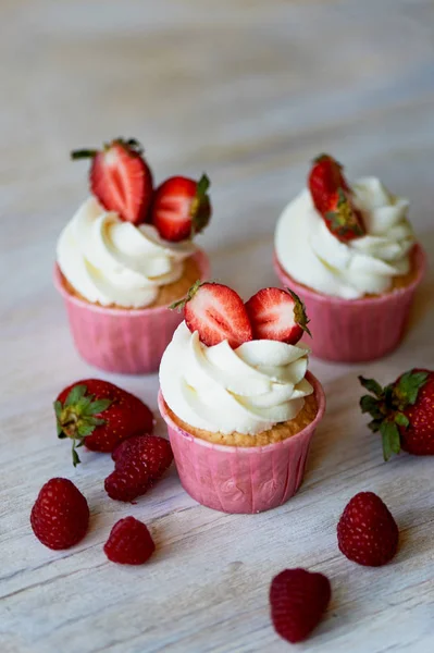 Cupcakes cu frisca si crema dulce, decorate cu capsuni. Pe un fundal de lemn deschis . — Fotografie, imagine de stoc