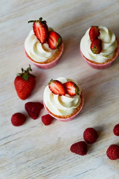 Cupcakes con crema batida y crema dulce, decorados con fresas. Sobre un fondo de madera claro . — Foto de Stock
