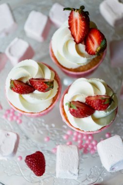Krem şanti ve tatlı ile cupcakes krem, çilek ile dekore edilmiştir. Bir cam stand, marshmallow ile