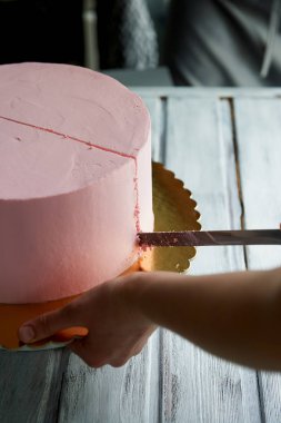 Pasta şefi pasta uzun bir bıçak ile kesmek. El bakımı. Süsler olmadan minimalist tarzda bir pembe pasta kesme.