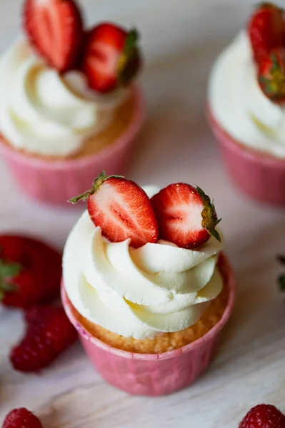 Cupcakes cu frisca si crema dulce, decorate cu capsuni. Pe un fundal de lemn deschis . — Fotografie, imagine de stoc