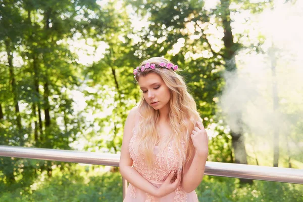 Портрет красивої нареченої блондинки в рожевому мереживному платті, прикраса для волосся, ручної роботи. Ніжність. Встановлення сонця підсвічує хмари диму біля обличчя — стокове фото