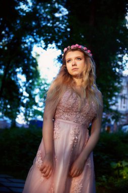 Pembe dantel elbise, saç dekorasyon, el yapımı bir güzel gelin sarışın kız portresi. Hassasiyet. Karanlık bir orman batan güneşin ışınları yeşil ortasında duruyor. Prenses
