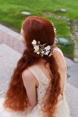 Güzel kızıl saçlı gelin geri oturur. Biraz görünür profil. El yapımı takı ile uzun kıvırcık saç.