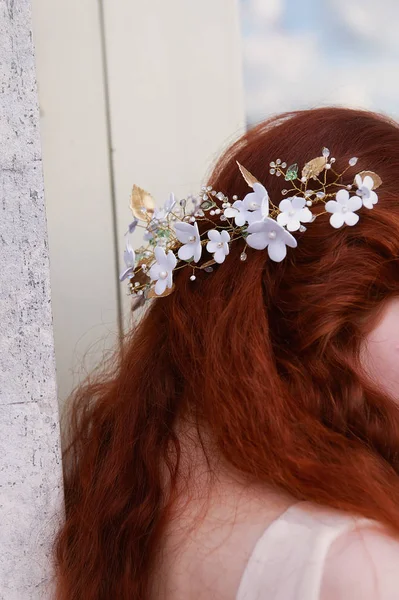 Beautiful red-haired bride sits back .Slightly visible profile. Long curly hair with handmade jewelry.
