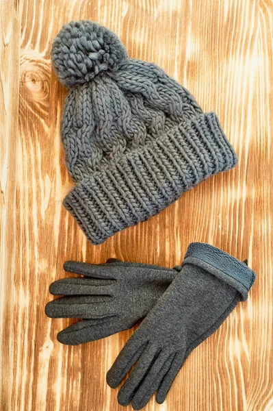 grey hat and gloves knit on a wooden surface.The concept is to keep warm in autumn or winter day