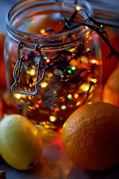 New years table.Garland, glowing in a glass jar. Among the citrus — Stock Photo, Image
