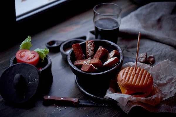 Burger with garlic croutons in the dark interior of the pub. Hearty, quick lunch.Atmospheric photo. Dark beer. — Stock Photo, Image