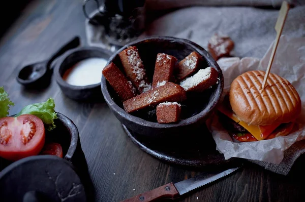 Burger with garlic croutons in the dark interior of the pub. Hearty, quick lunch.Atmospheric photo — Stock Photo, Image