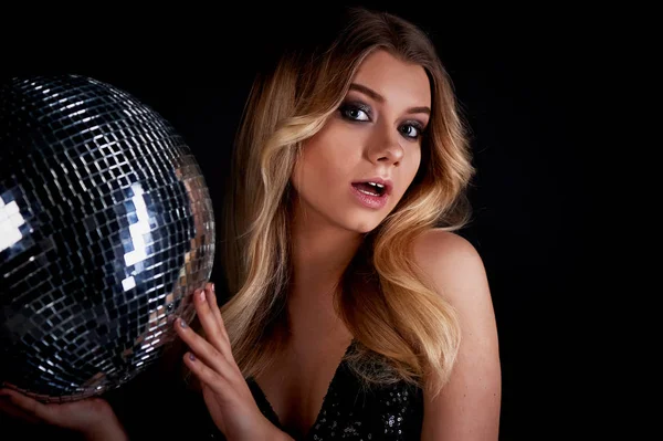 The blonde laying in the style of Abba holds a disco ball. The era of disco.Night club, dancing