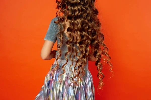 Ragazza su sfondo arancione nello Studio. Capelli ricci molto lunghi come in una fiaba. sviluppo nel movimento — Foto Stock