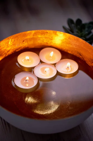 Zlatá miska s vodou ve které plovoucí svíčky. Interiérové dekorace pro uvolněnou atmosféru — Stock fotografie